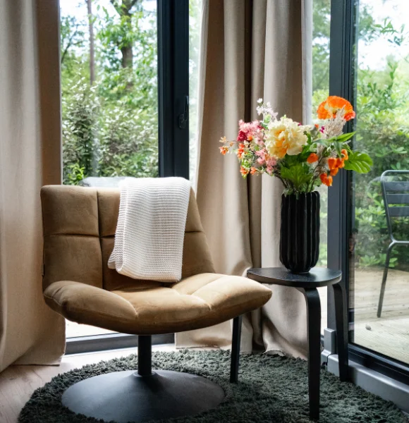 Stoel met boeket en uitzicht op de tuin in Tiny House Onyx, midden in de Veluwe